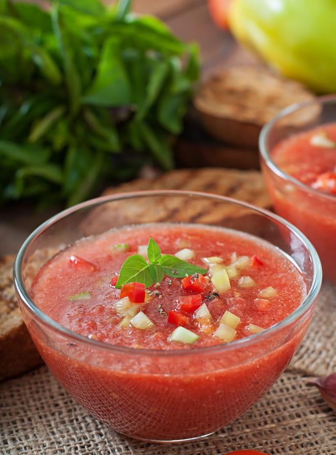 Tazón de gazpacho fresco decorado con trozos de verdura y albahaca